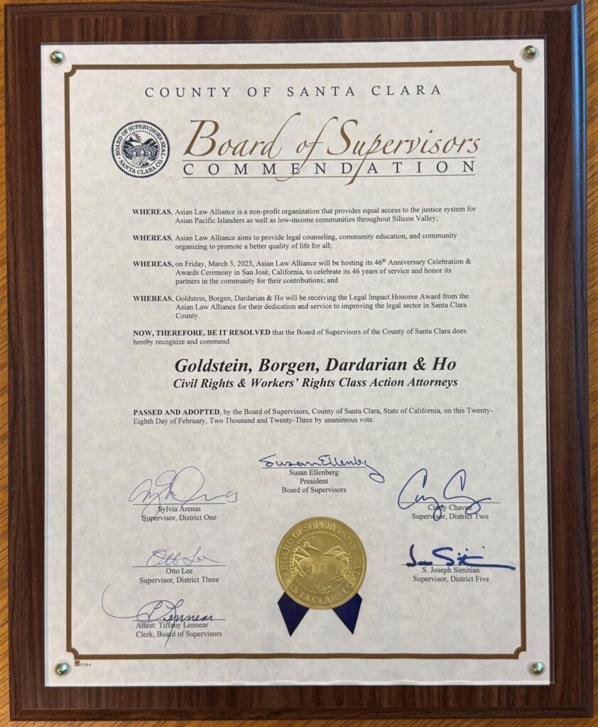 Asian Law Alliance County of Santa Clara Board of Supervisors Commendation, 2023 A framed award of Board of Supervisors Commendation from the County of Santa Clara, mounted on a wooden wall or tabletop. The award is enclosed in a large, rectangular dark reddish-brown wood frame with visible wood grain. The frame has a raised, beveled inner edge. The certificate is mounted behind a clear protective surface and secured at its four corners with small round metallic fasteners. The award is printed on an off-white, slightly mottled paper with a thin brown decorative border and ornamental corner details. At the top, centered, it reads: COUNTY OF SANTA CLARA Below that is a large script heading: Board of Supervisors COMMENDATION A circular Board of Supervisors Santa Clara County seal appears to the left of the heading. underneath it states: WHEREAS, Asian Law Alliance is a non-profit organization that provides equal access to the justice system for Asian Pacific Islanders as well as low-income communities throughout Silicon Valley; WHEREAS, Asian Law Alliance aims to provide legal counseling, community education, and community organizing to promote a better quality of life for all; WHEREAS, on Friday, March 3, 2023, Asian Law Alliance will be hosting its 46th Anniversary Celebration & Awards Ceremony in San José, California, to celebrate its 46 years of service and honor its partners in the community for their contributions; and WHEREAS, Goldstein, Borgen, Dardarian & Ho will be receiving the Legal Impact Honoree Award from the Asian Law Alliance for their dedication and service to improving the legal sector in Santa Clara County. NOW, THEREFORE, BE IT RESOLVED that the Board of Supervisors of the County of Santa Clara does hereby recognize and commend Goldstein, Borgen, Dardarian & Ho Civil Rights & Workers’ Rights Class Action Attorneys Below this is the statement, indicating that the commendation was passed and adopted by the Board of Supervisors of the County of Santa Clara, State of California, on February 28, 2023. The lower portion contains handwritten signatures and printed titles for members of the Board of Supervisors, including: Susan Ellenberg, President, Board of Supervisors Sylvia Arenas, Supervisor, District One Cindy Chavez, Supervisor, District Two Otto Lee, Supervisor, District Three S. Joseph Simitian, Supervisor, District Five Tiffany Le (shown as attesting), Clerk, Board of Supervisors A large gold-colored embossed Board of Supervisors, Santa Clara County seal with two dark-blue ribbon tails is positioned near the bottom center.